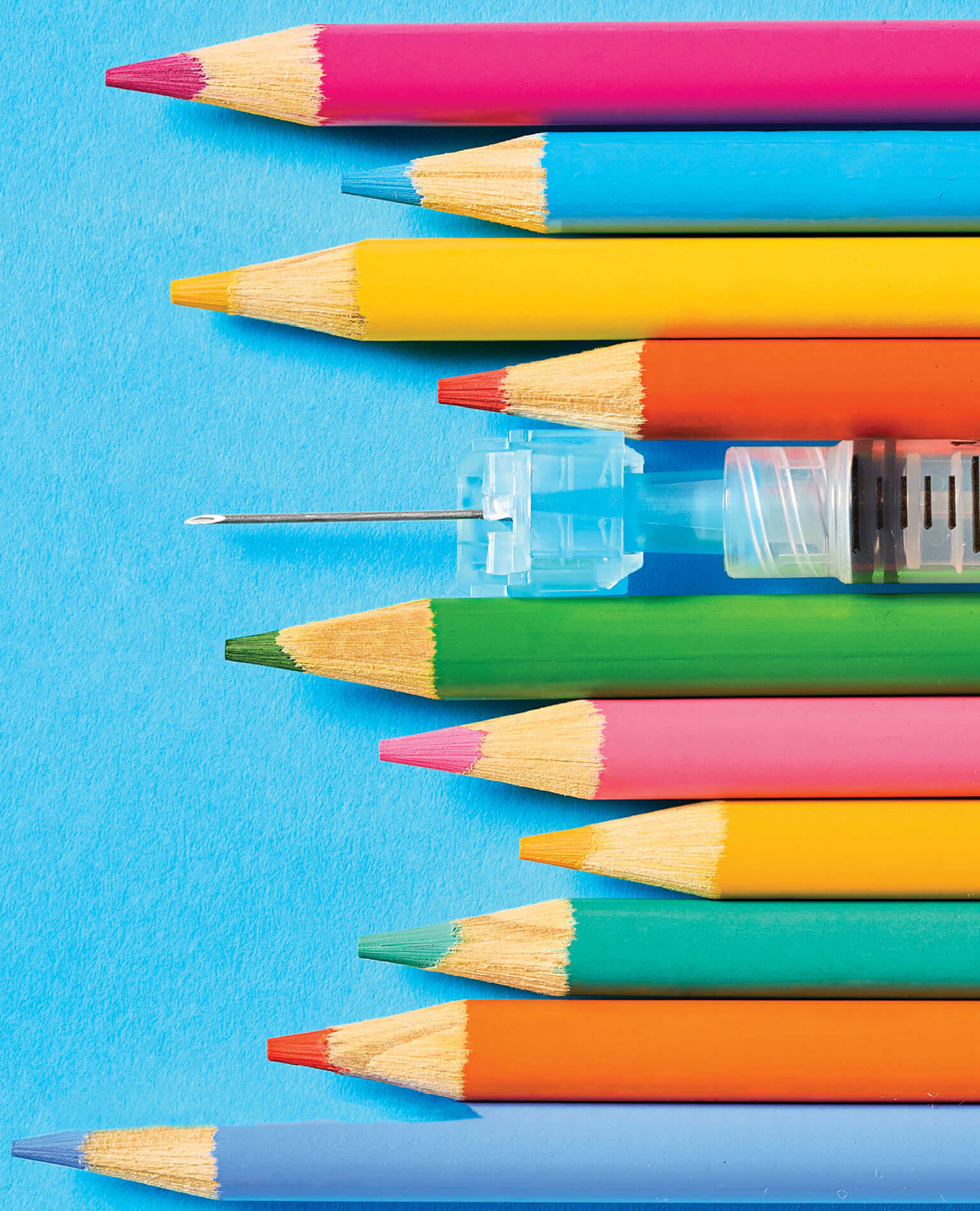 A series of colored pencils lined up with a hypodermic needle.