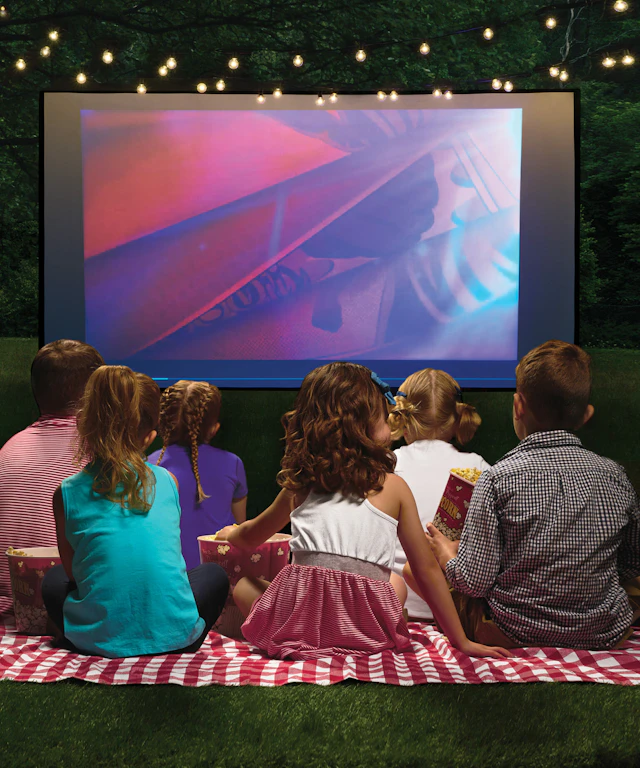 Children sitting on ground in the backyard watching an outdoor movie screen