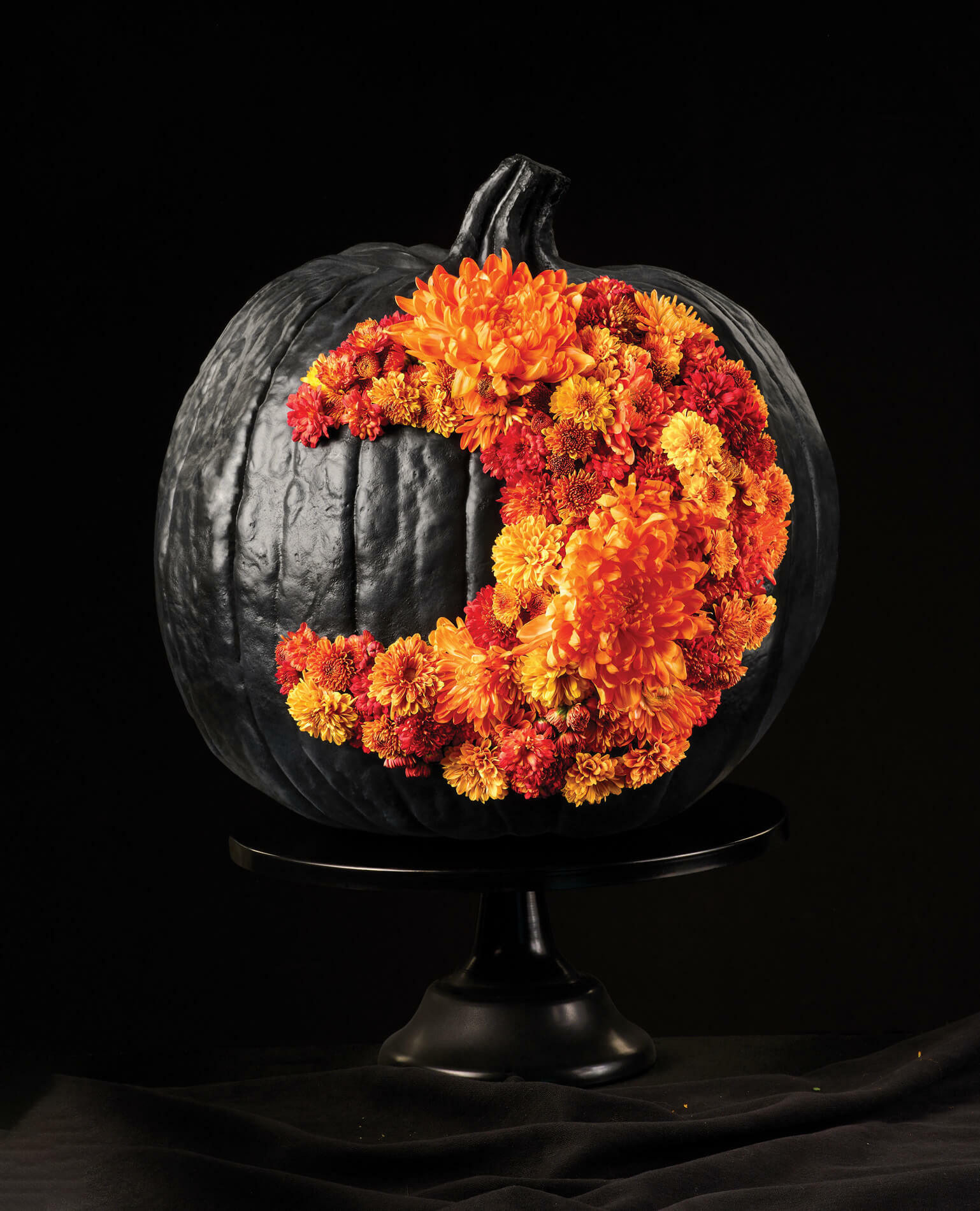 A crescent moon made from orange flowers adorns a pumpkin painted all black.