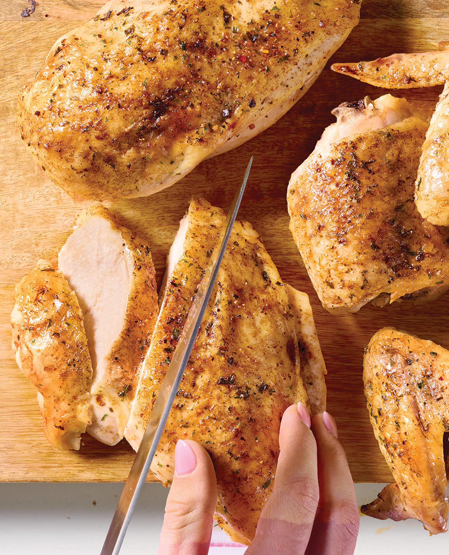A woman breaking down a whole chicken, cutting the breast with a knife.