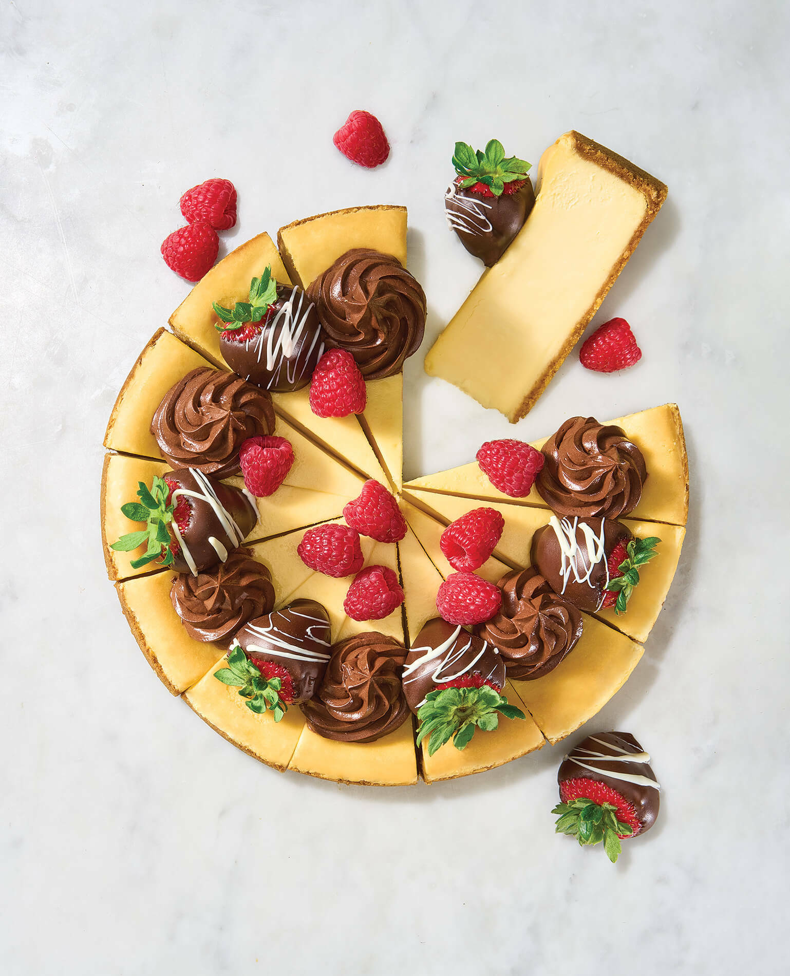 A cheesecake topped with chocolate-covered strawberries and raspberries.