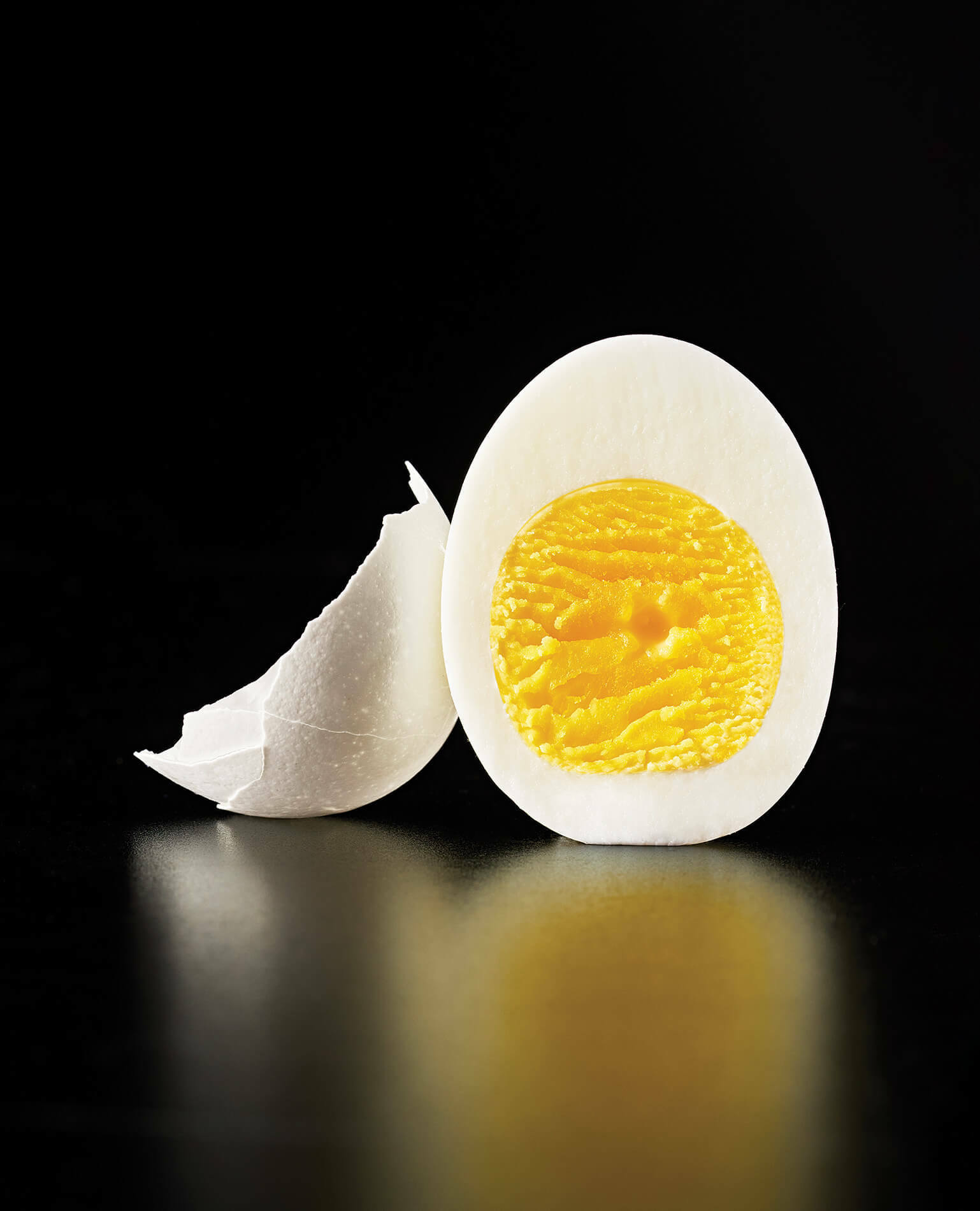 A sliced hard boiled egg on a reflective black background.
