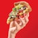 A woman's hand holding a slice of pizza on a red background.