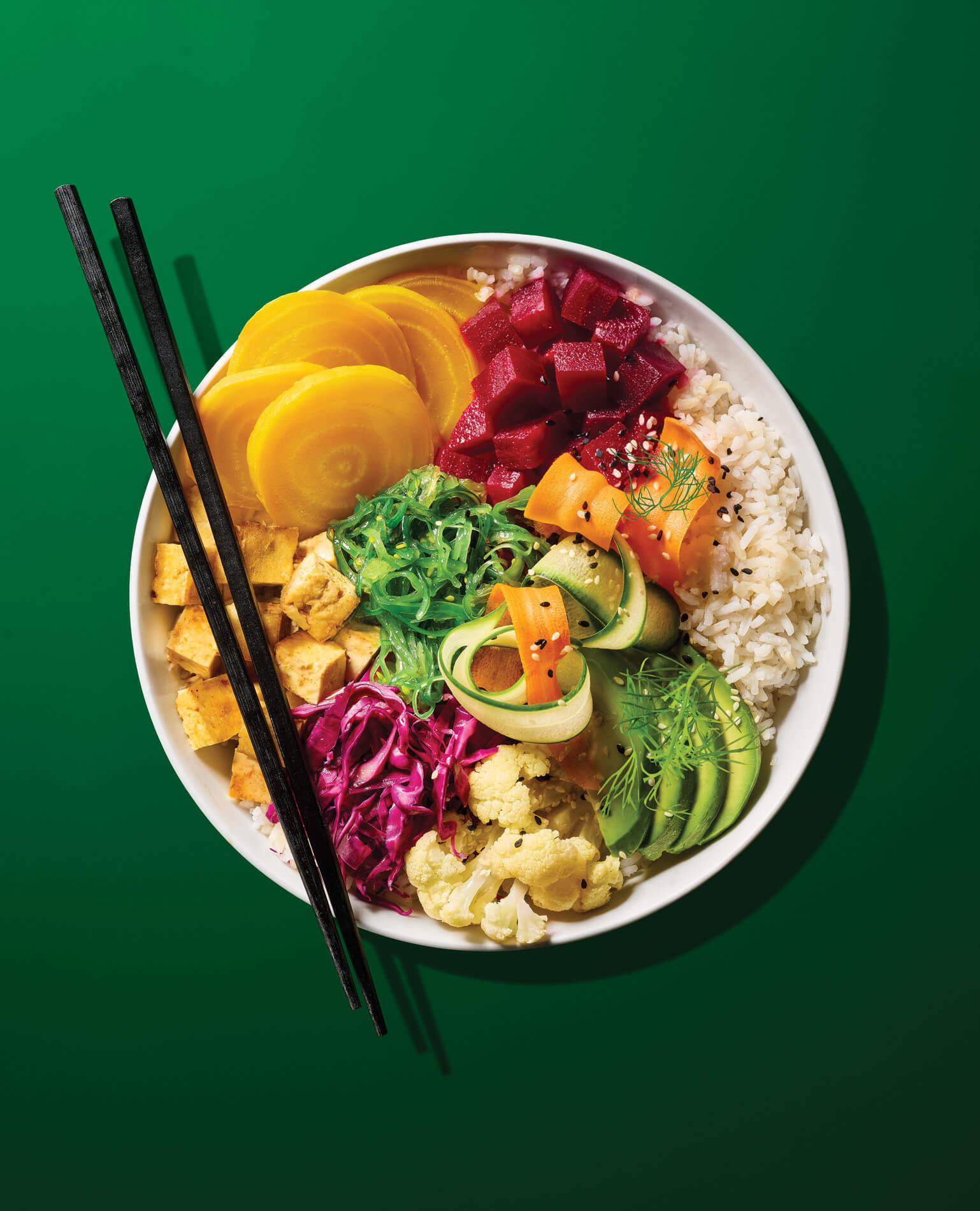 A brightly colorful poke bowl on a green background with chopsticks.