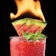 A red cocktail with a flaming watermelon wedge as garnish.