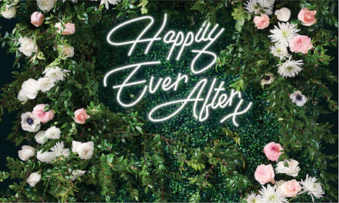 A floral wall with the words Happily Ever After in cursive neon lighting.