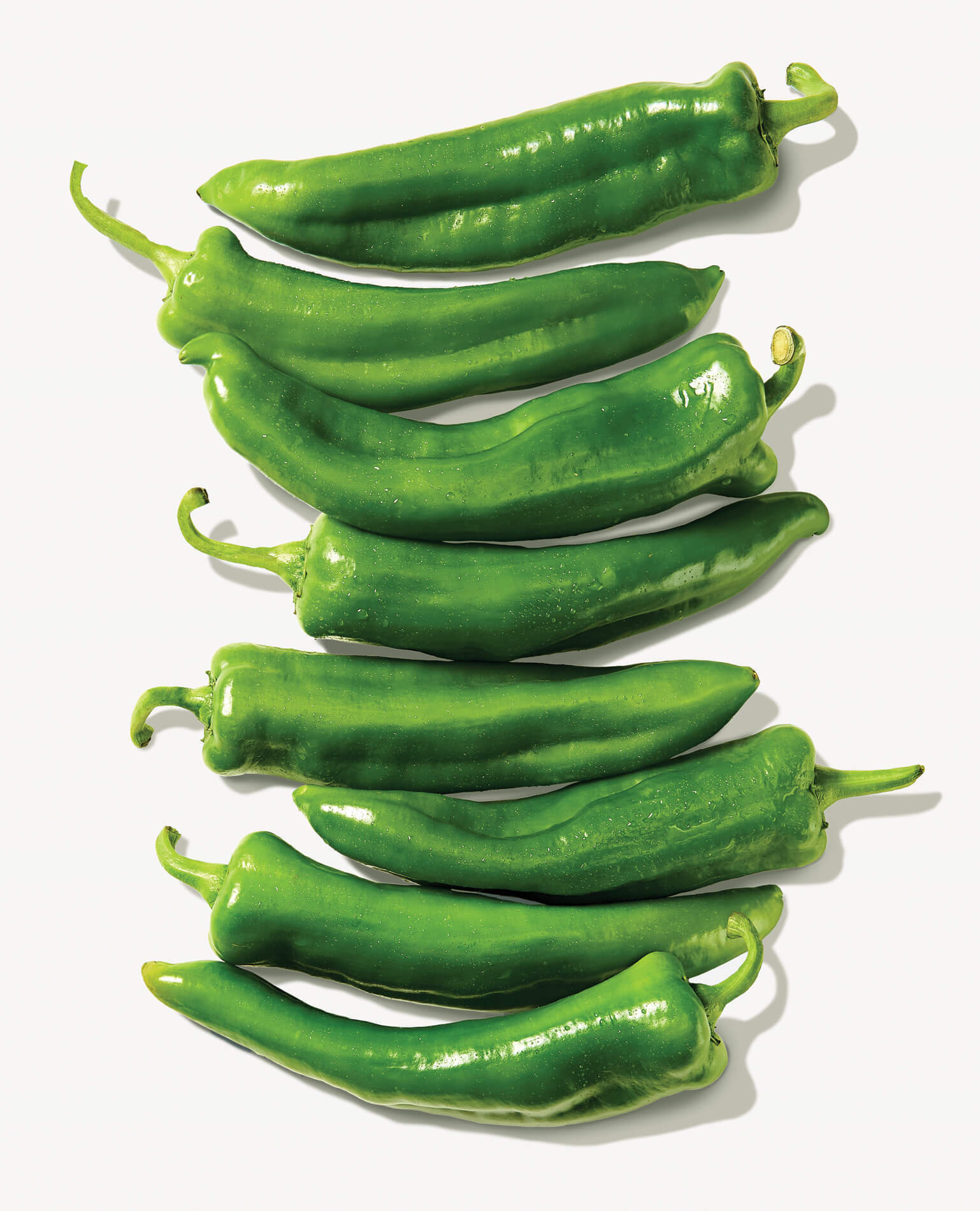 Eight hatch peppers on a light gray background.