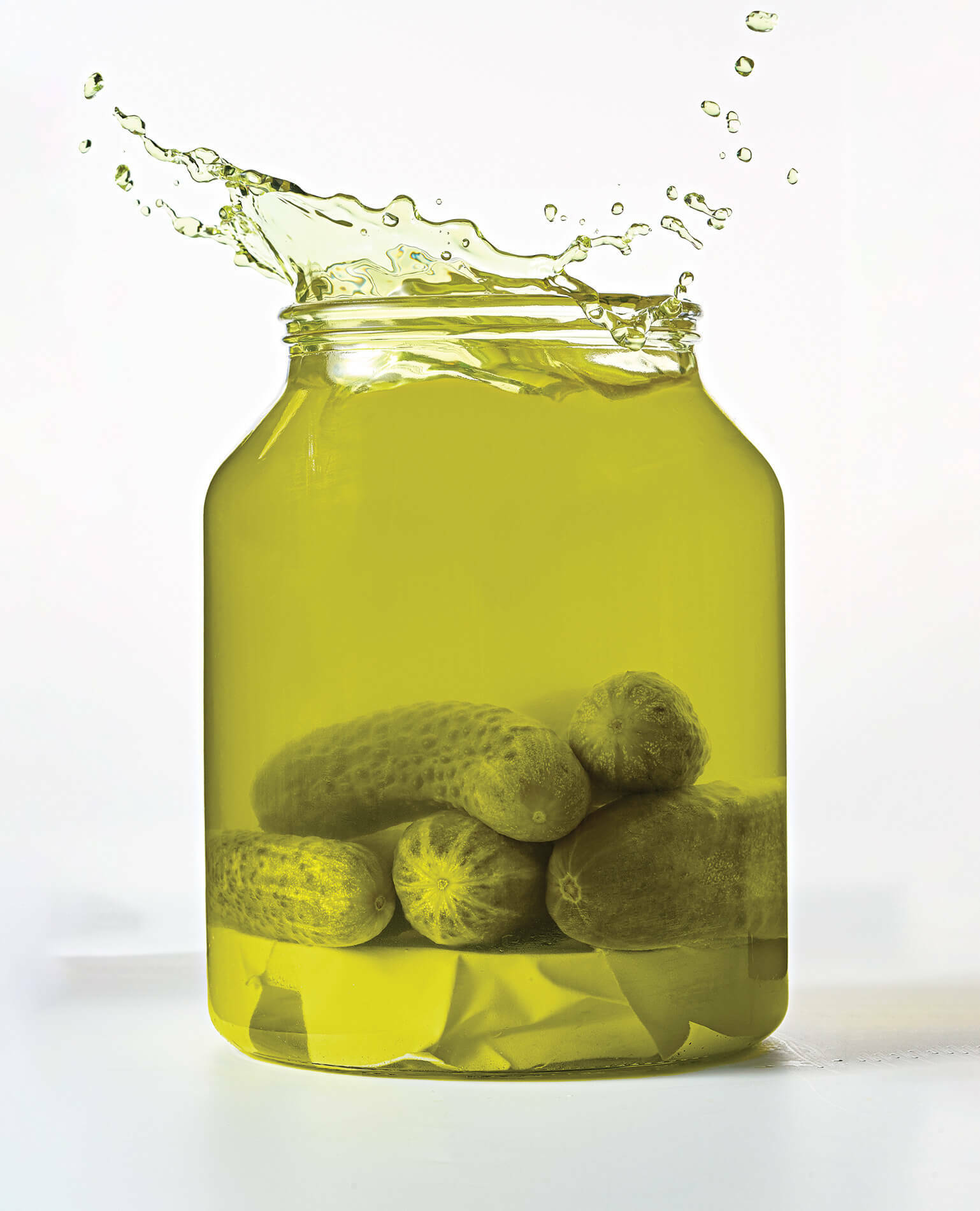 A large jar of dill pickles with pickle juice splashing out of the top.