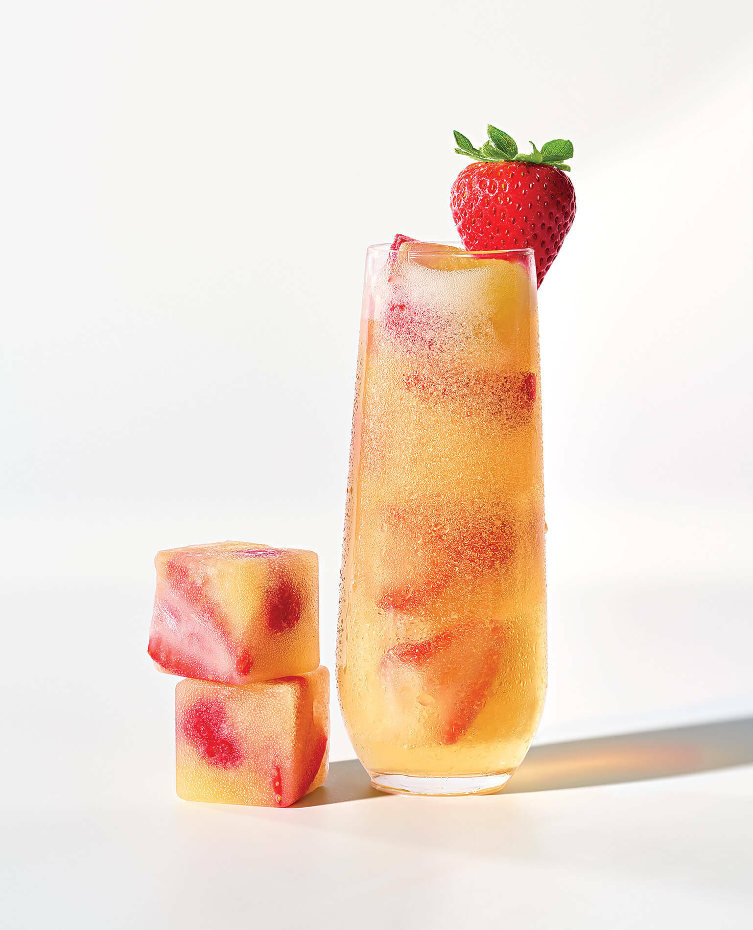 Mimosa ice cubes stacked next to a glass of a mimosa cocktail.