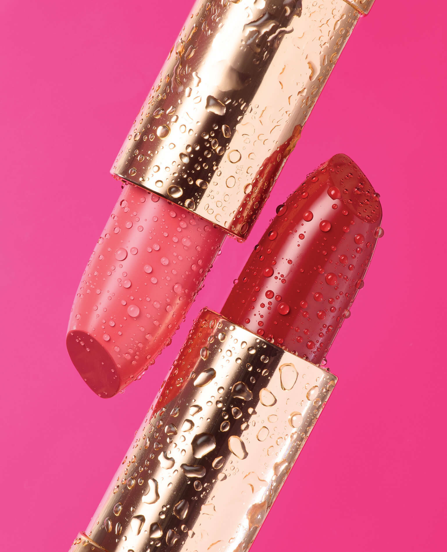 A red and a pink shade of lipstick on a pink background.