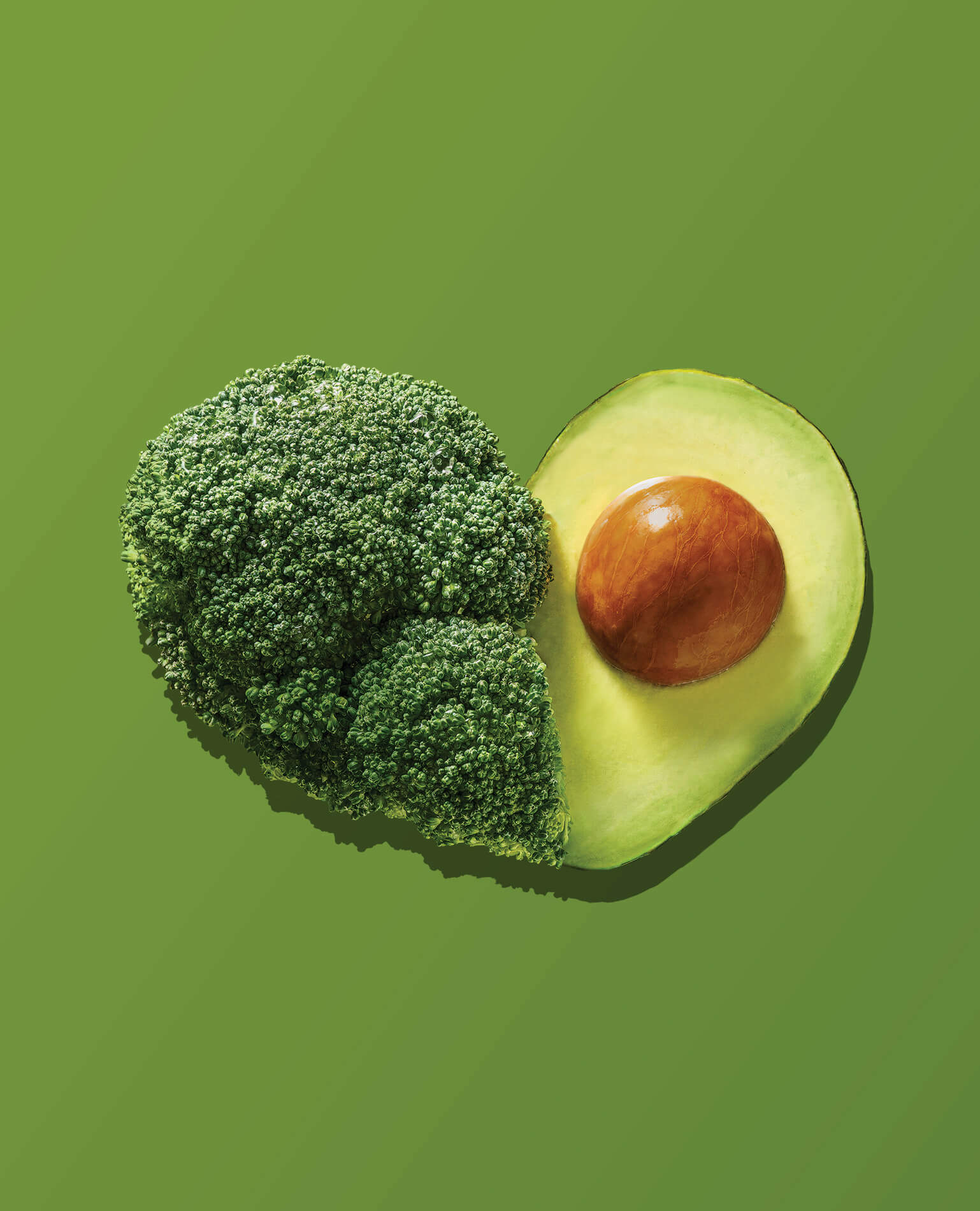 A heart made from a head of broccoli and a cut avocado on a green background.