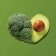 A heart made from a head of broccoli and a cut avocado on a green background.