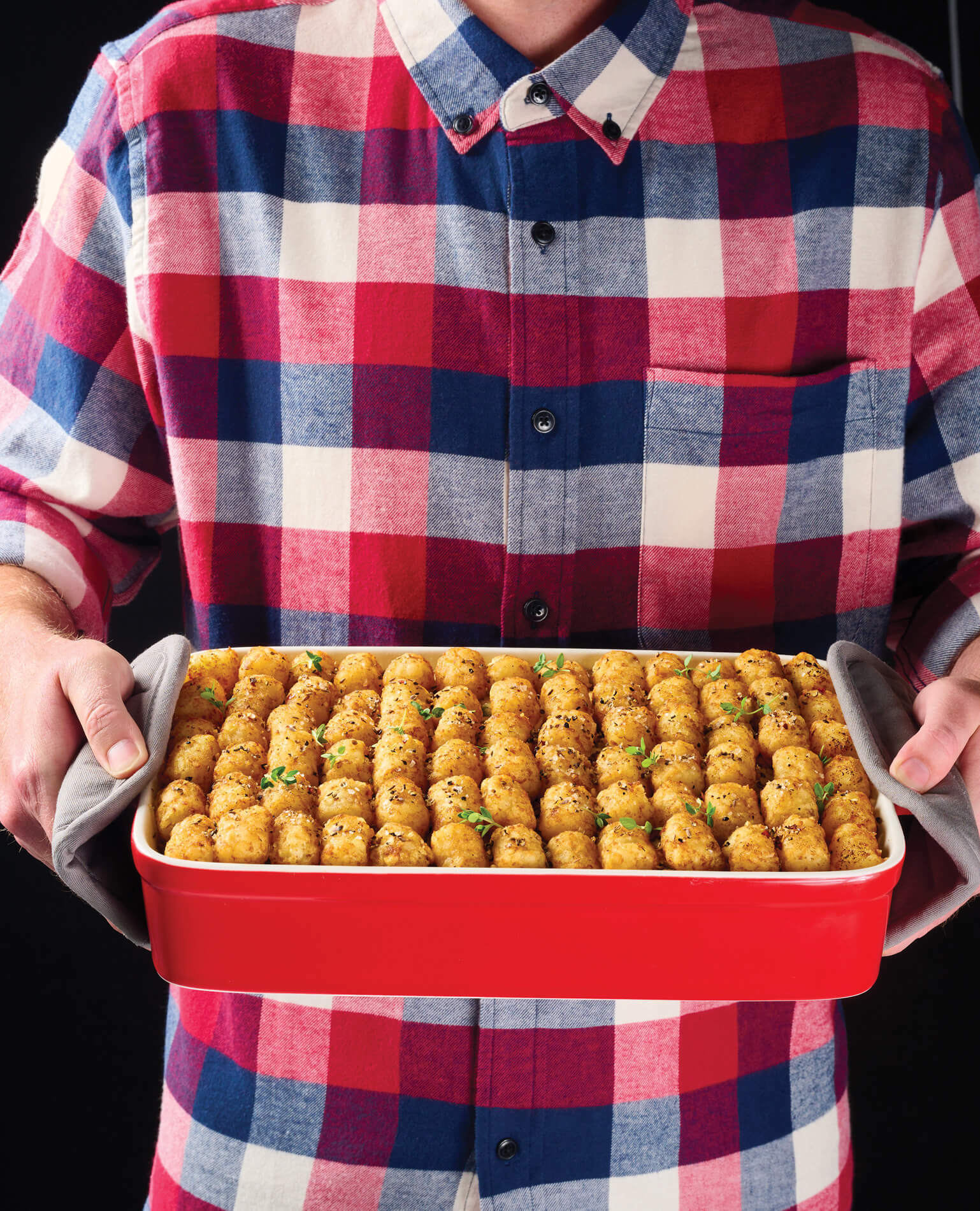 A man in a flannel shirt holding a casserole dish of hot dish.