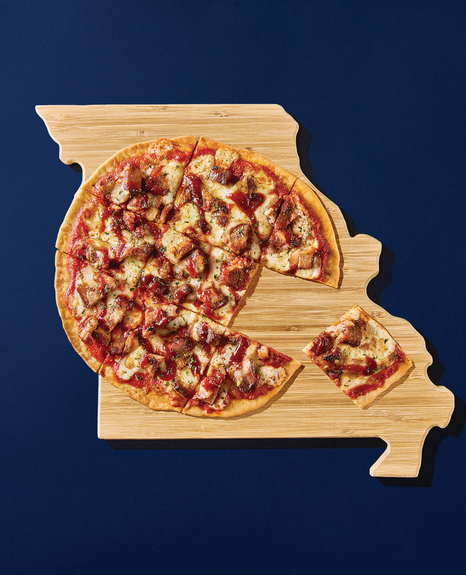 A BBQ pizza sitting on a wooden plate in the shape of the state of Missouri.