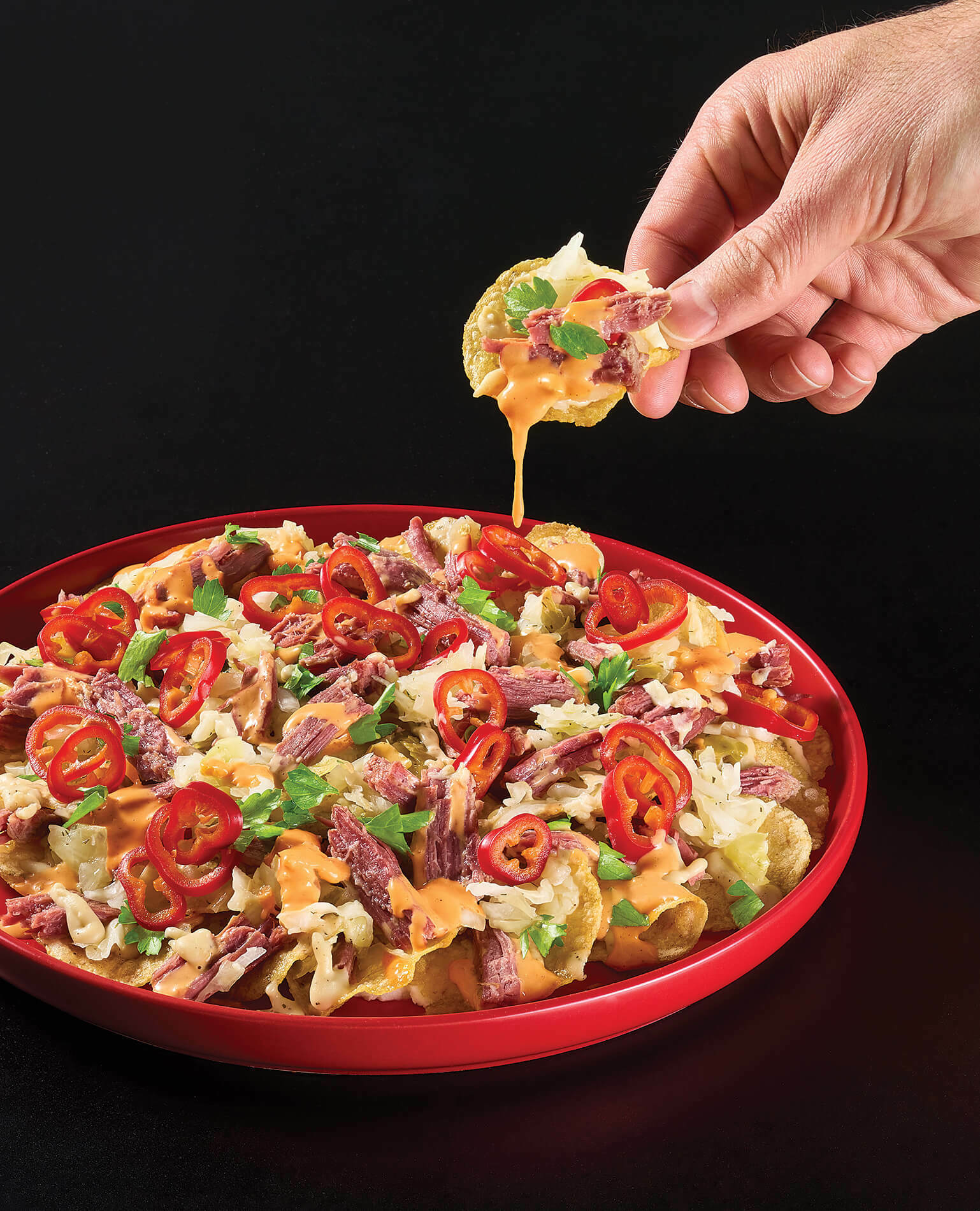 A hand pulling a chip out of a plate of Irish Nachos.