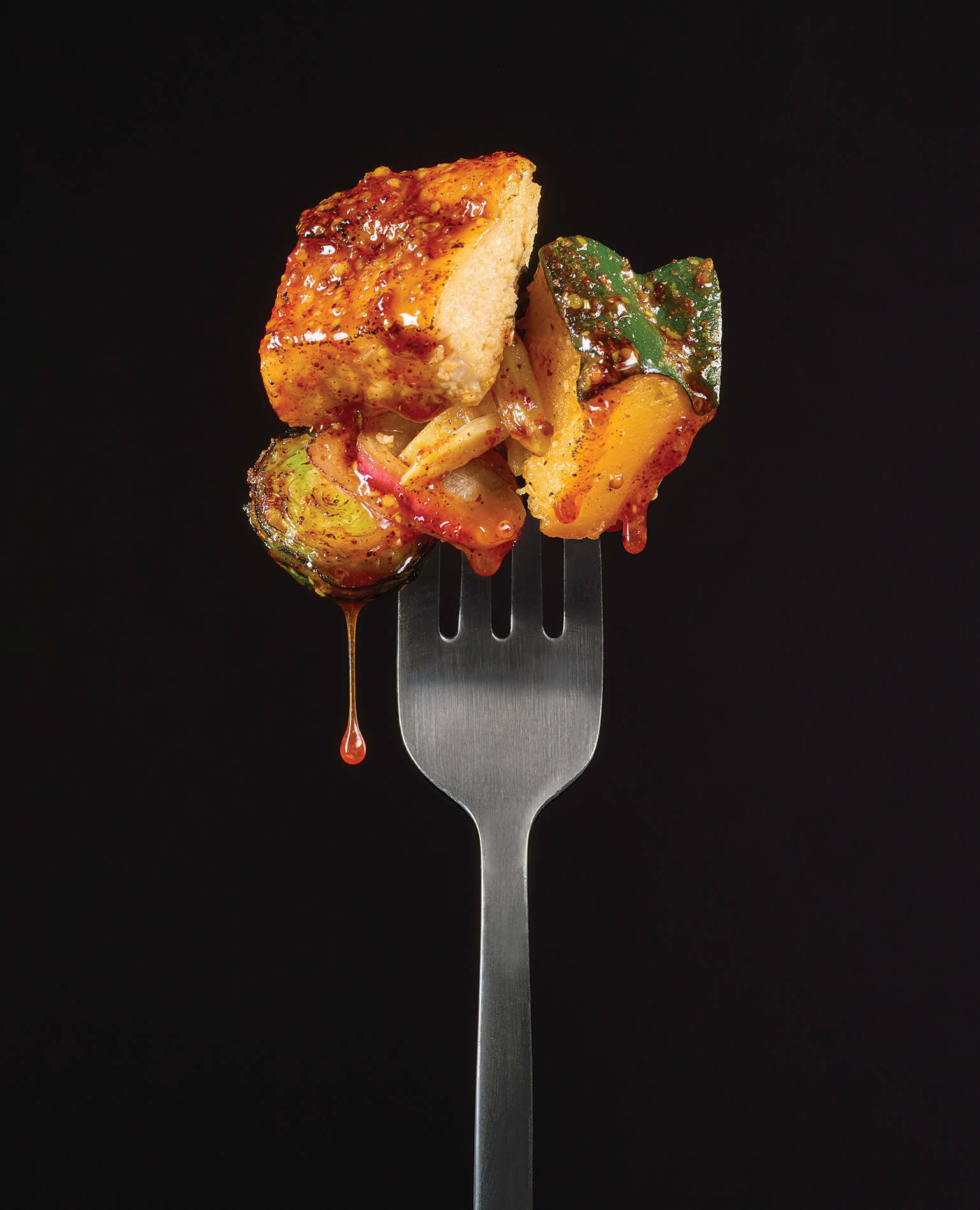 A forkful of juicy chicken on a black background.