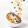 Blueberries, granola, and almond slivers falling into a bowl of oatmeal.