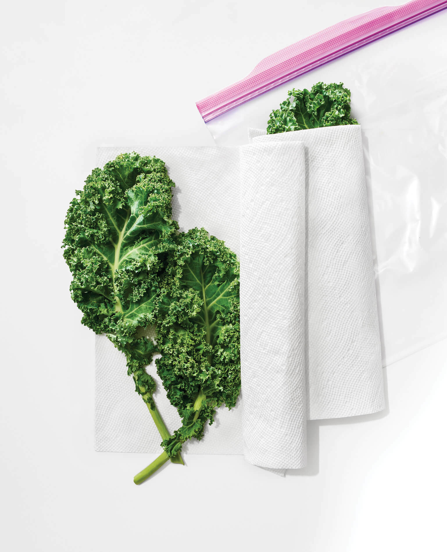 Some kale leaves wrapped in paper towels inside a sealed plastic bag.