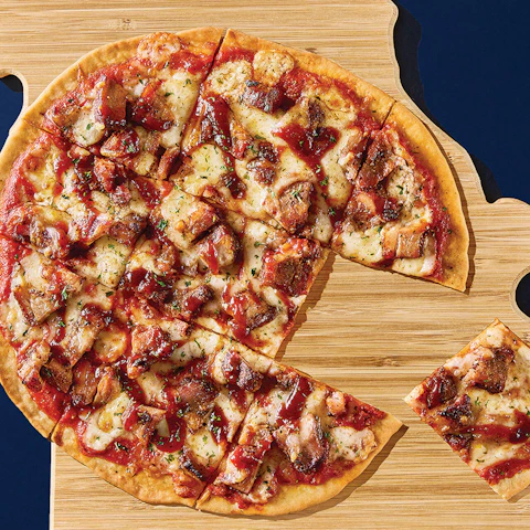 A St Louis Style BBQ Pizza sliced and placed on a wooden pallet shaped like the state of Missouri
