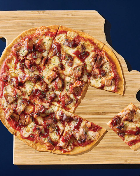 A St Louis Style BBQ Pizza sliced and placed on a wooden pallet shaped like the state of Missouri