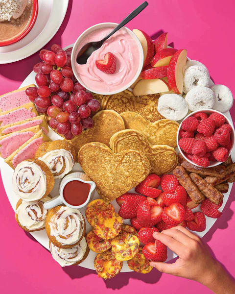 A charcuterie board filled with Valentine's Day breakfast items such as heart-shaped pancakes, strawberries, mini egg bites, etc.