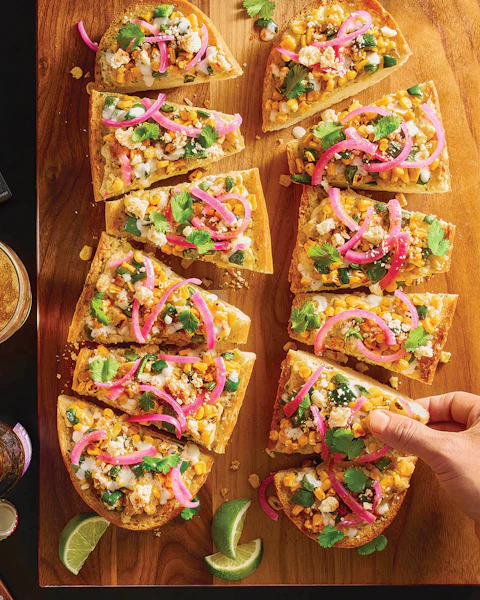 A hand selecting a piece of Elote Garlic Bread with Pickled Onions