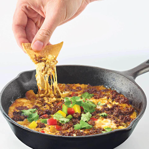 A hand dipping a chip into a skillet of Queso Fundido