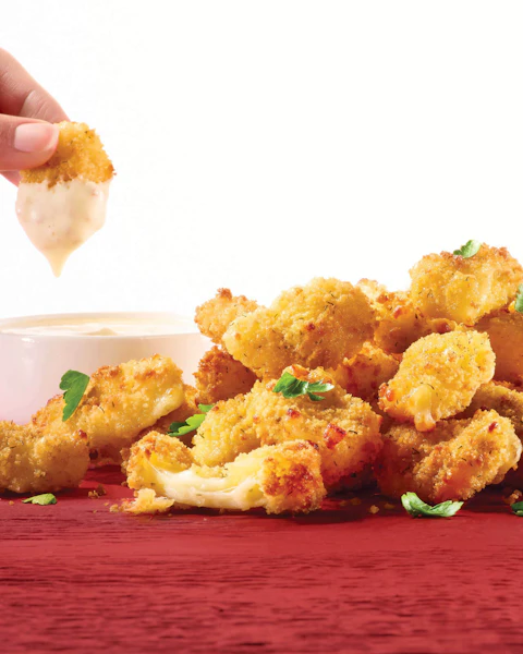 A hand dipping Air Fried Triple Ranch Cheese Curds in ranch dressing