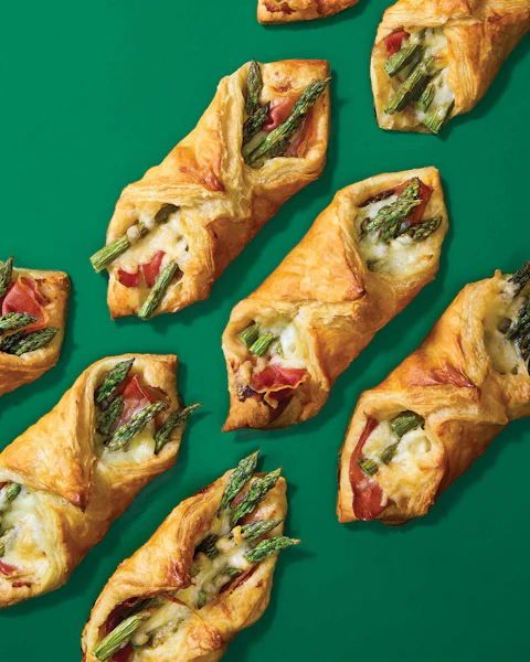 Rows of Asparagus Prosciutto Puff Pastry on a green background.