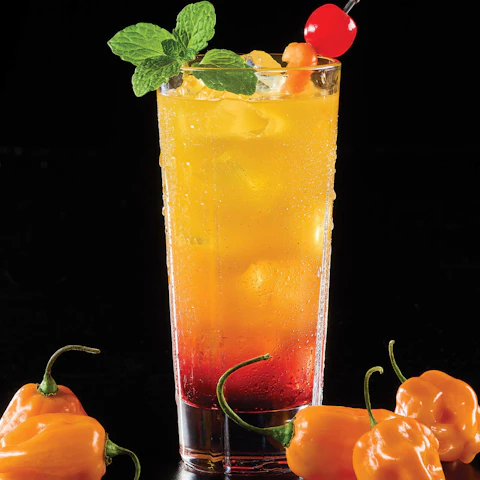 Glass of Hot Tequila Sunrise cocktail surrounded by habanero peppers.