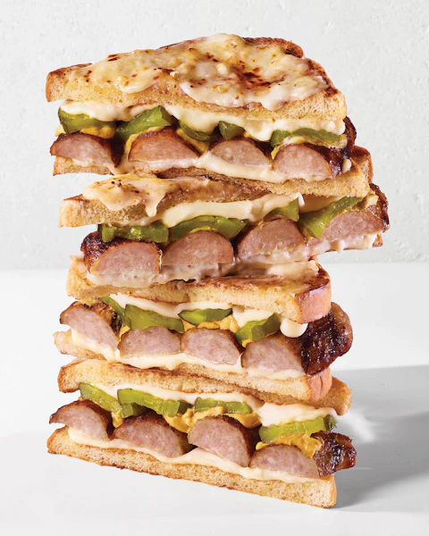 Halves of a Hot Brat Croque Monsieur sandwich stacked up on a white background.