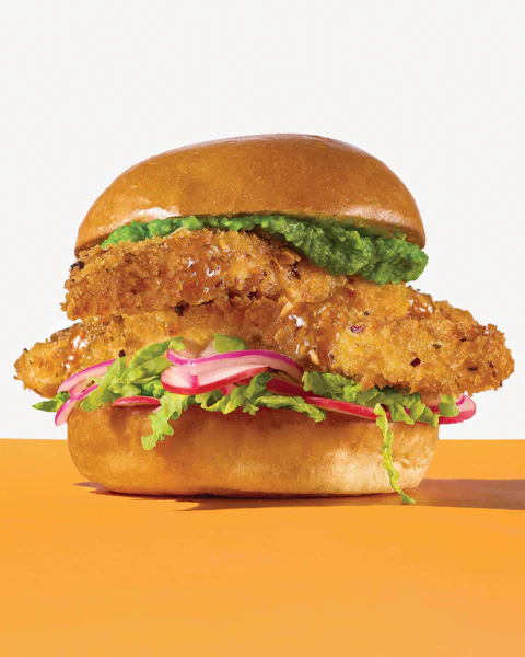 An Air Fried Fish Sandwich on a orange surface.