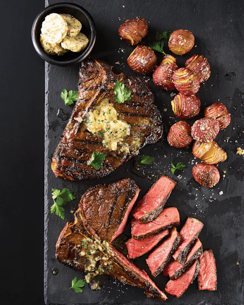 Serving platter of sliced T-Bone Steaks with a cup of Bourbon Compound Butter