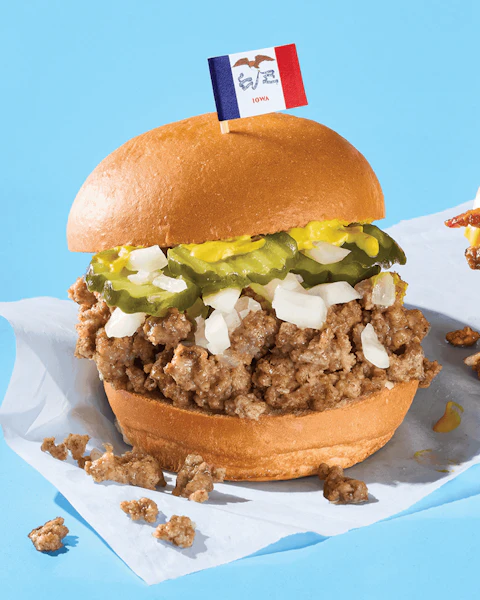 A Slow Cooker Loose Meat Sandwich with a tiny Iowa flag stuck in the top bun