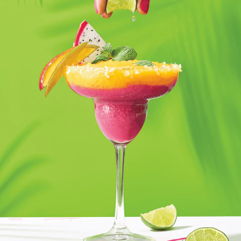 Hand squeezing lime into a colorful Tropical Dragon Fruit Blended Margarita