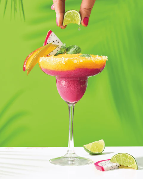 Hand squeezing lime into a colorful Tropical Dragon Fruit Blended Margarita