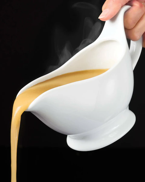 A hand pouring a gravy boat filled with All Purpose Gravy