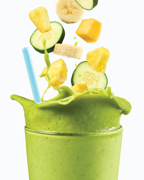 Glass of Pineapple Mango Cucumber Smoothie with ingredients plopping into it