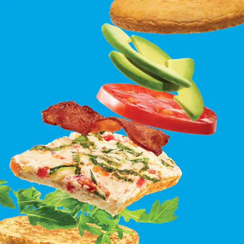 Layers of Sheet Pan Egg White Breakfast Sandwiches flying apart on a blue background