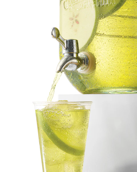 A glass of Whiskey Green Apple Punch being poured from large container