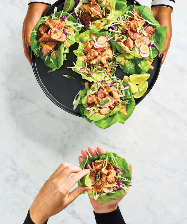 Hands taking a lettuce wrap from a tray of lettuce wraps
