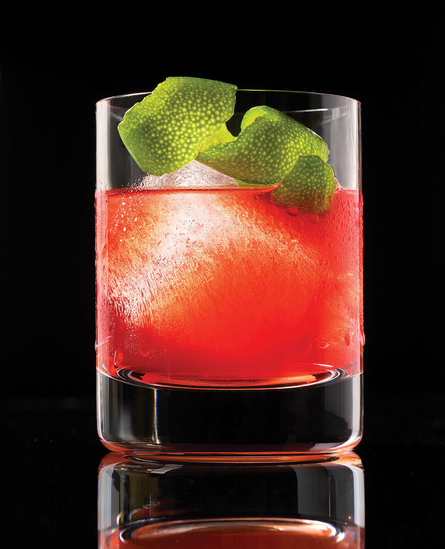 A Red Irish cocktail glass with a lime garnish on a black background.