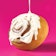 A cinnamon roll being drizzled with frosting on a pink background.