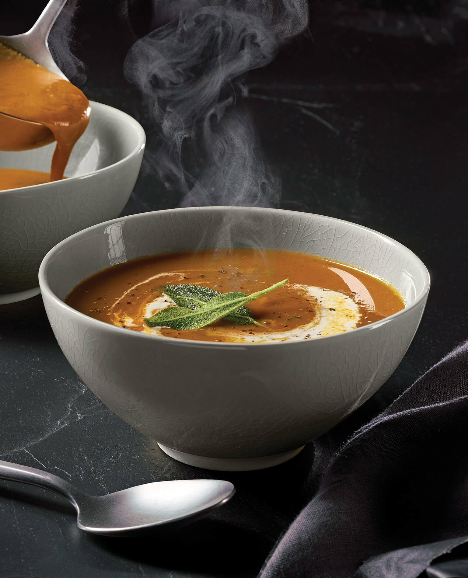 A bowl of steaming Sweet Potato soup on a black background