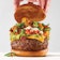 A thick cheeseburger stacked with guacamole and tater tots, with a hand lifting the top bun.