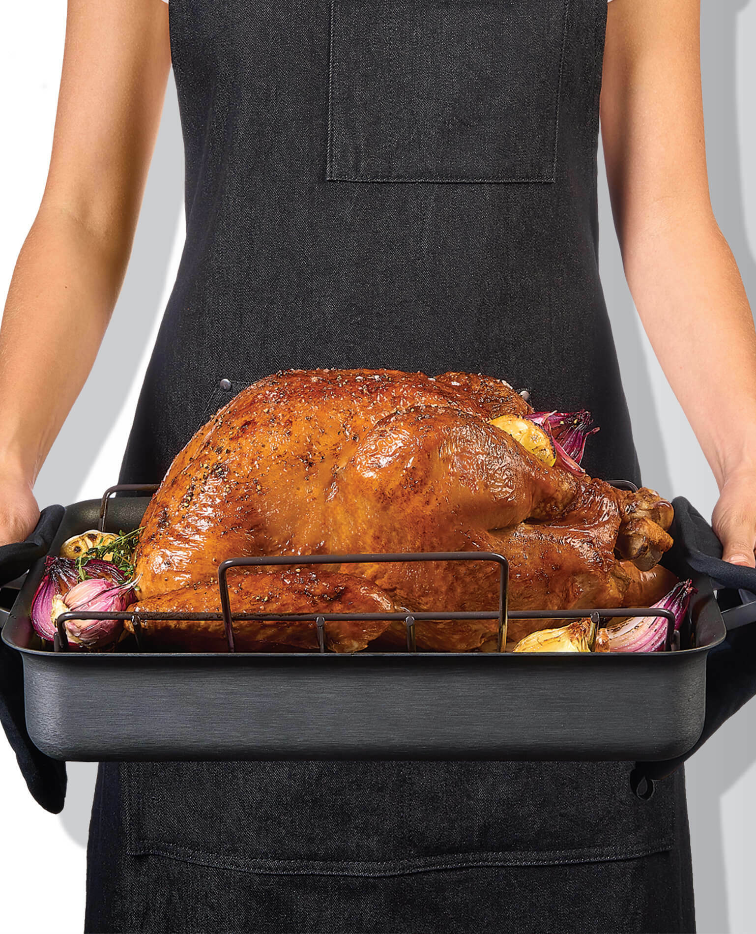 A woman holding a roasting pan of a Thanksgiving turkey, ready to be carved.