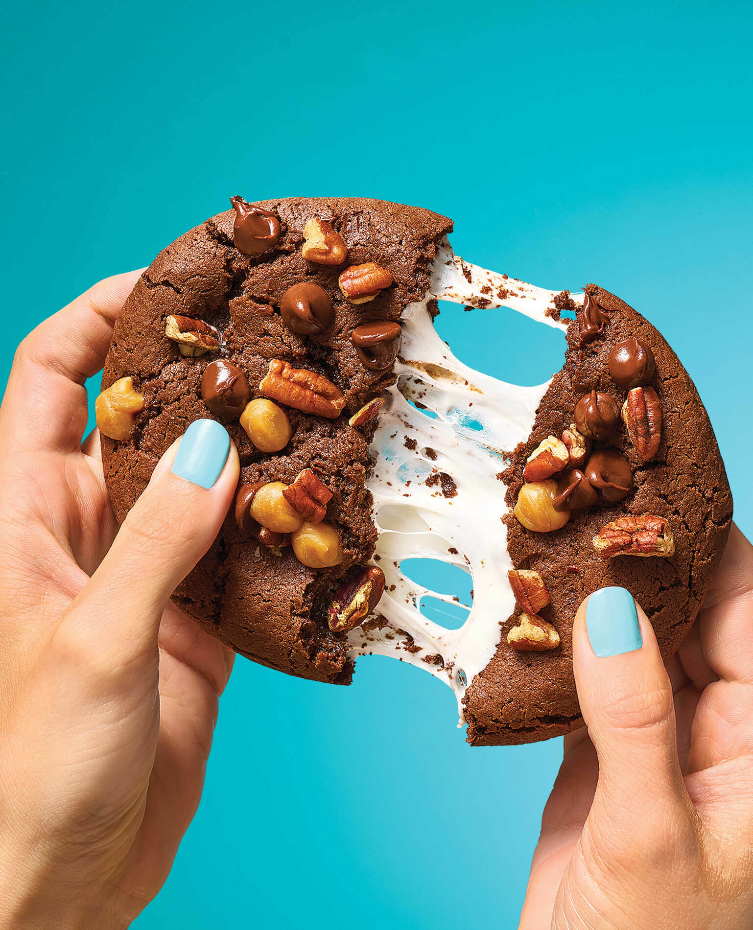 A woman's hands pulling apart a gooey chocolate cookie stuffed with marshmallow.