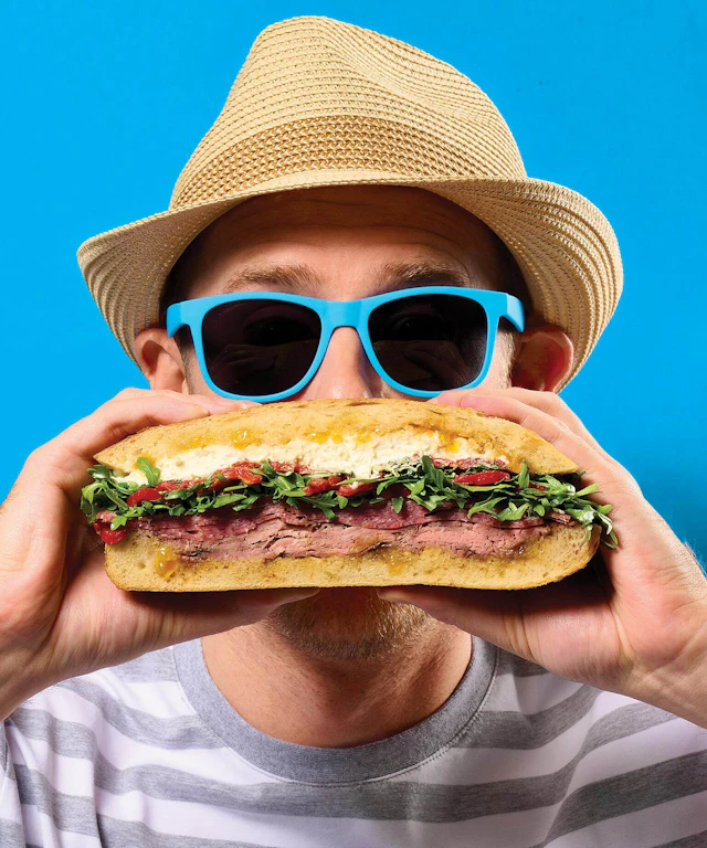 Man in hat and glasses eating large sandwich