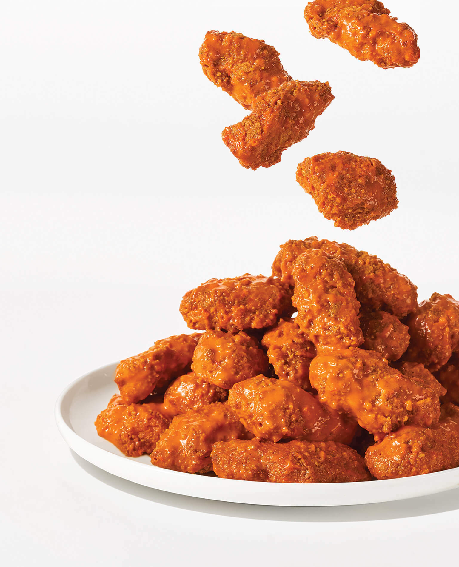 Baked buffalo wings falling onto a white plate.